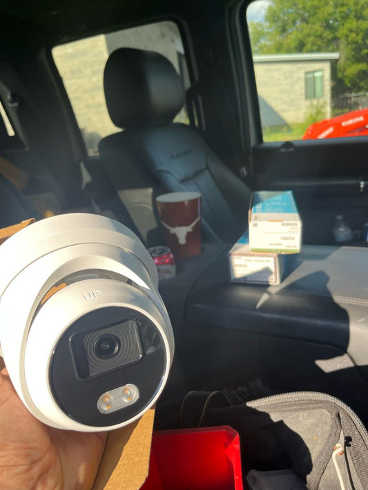 Commercial video surveillance cameras covering a Texas storefront at night, shown with remote viewing on a smartphone—installed and maintained by Avenger Security.